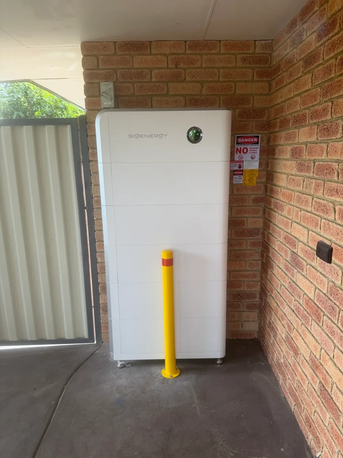 A home battery against a brick wall at a Leeming home, with a protective bollard in front, installed by SolArk Electrical