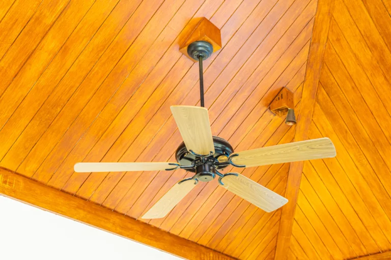 A close-up of a ceiling fan on a wooden ceiling.