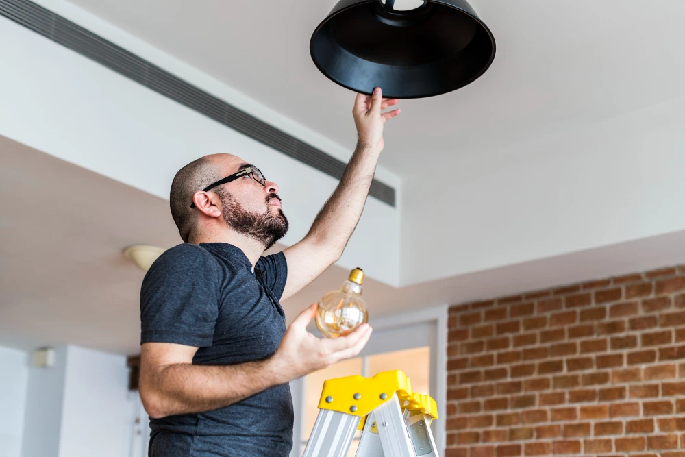 A man performing a lighting installation by changing a light bulb.