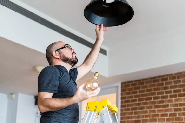A man standing on a ladder changing a lightbulb.