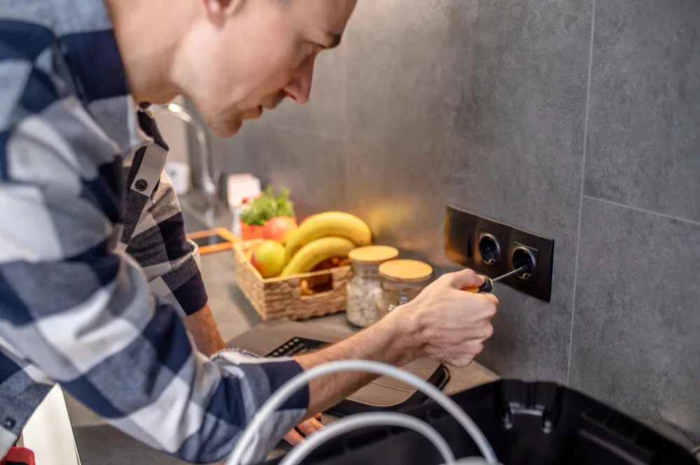 A man inspecting an electrical socket of a modern kitchen.