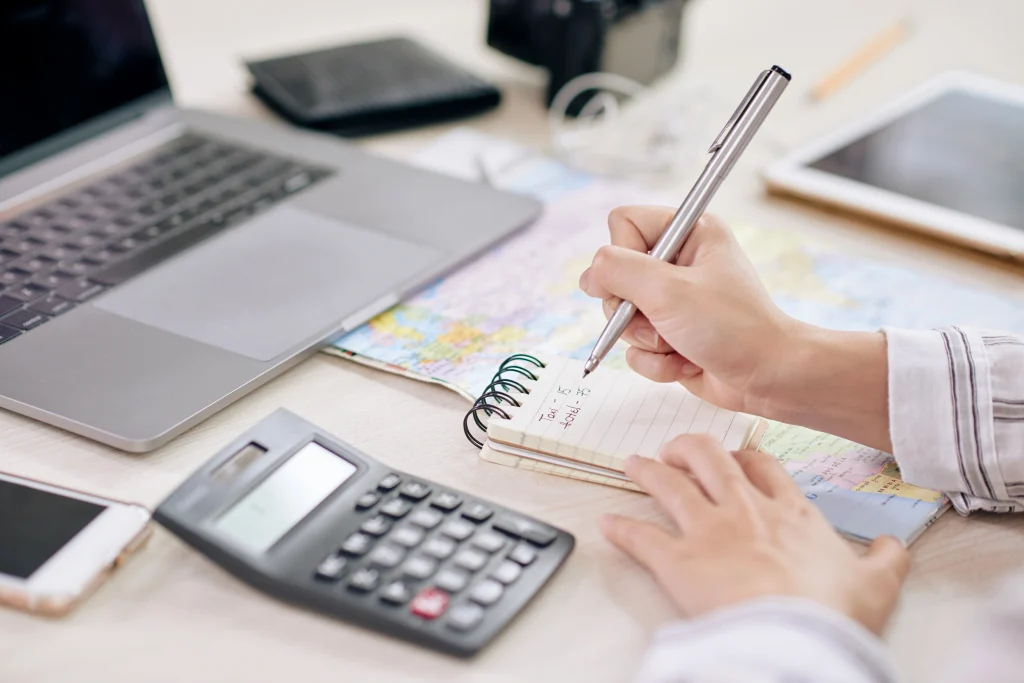 A homeowner planning a solar power investment in Mandurah by taking notes at a desk with a laptop, calculator, and map.