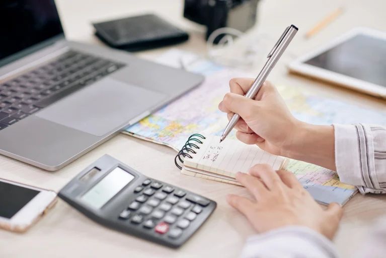 A homeowner planning a solar power investment in Mandurah by taking notes at a desk with a laptop, calculator, and map.