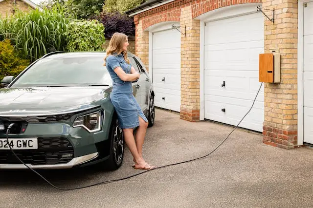 A woman charging her electric vehicle outside her garage.