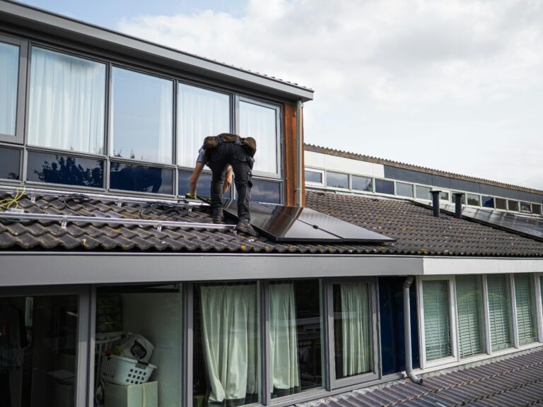 A solar electrician adjusts a solar panel on a tiled house roof.