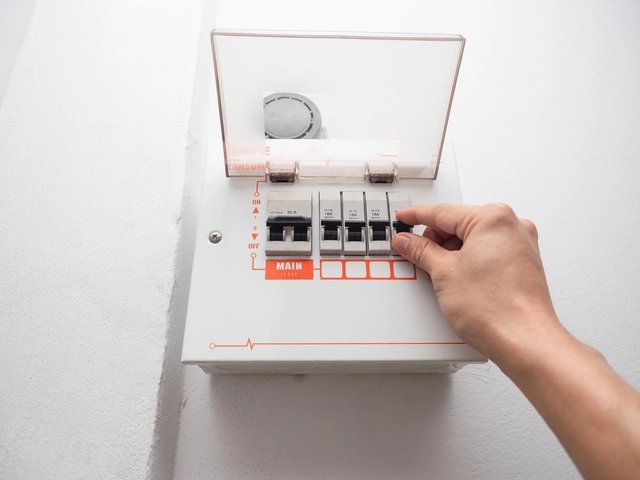 A hand checking an electric safety breaker on a white wall.