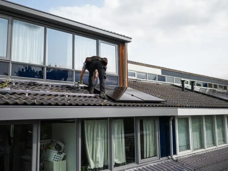 A solar electrician adjusts a solar panel on a tiled house roof